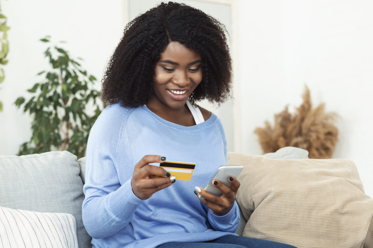 Black lady using phone and credit card on couch